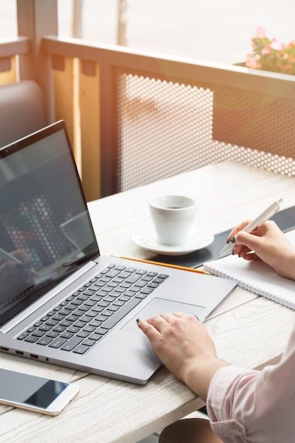 Premium Photo | Close up portrait of a young woman working on laptop and writing, coffee on the table.